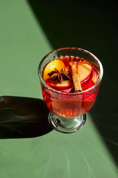 Baharatlı, elmalı ve portakallı sıcak şarap kadehleri yeşil arka planda. Tarçın, kakule ve anason ile geleneksel Noel içeceği. Yaratıcı Noel tebrik kartı.