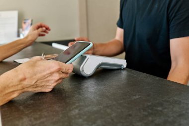 Otel resepsiyonunda kredi kartı okuyucu tarafından tanınmayan bir kadın cep telefonuyla ödeme yapıyor..