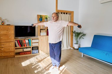 Olgun bir adam evde dambıllarıyla egzersiz yapıyor. Sağlık için sağlıklı bir yaşam tarzı.