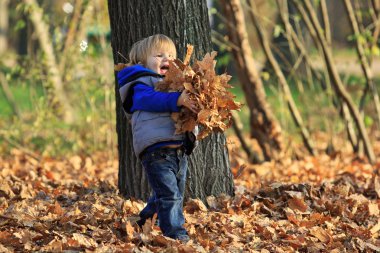 Çocuk parkta yapraklarla oynuyor.