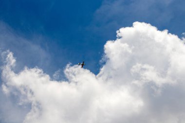 Mavi gökyüzüne karşı bulutların arasında küçük bir uçak