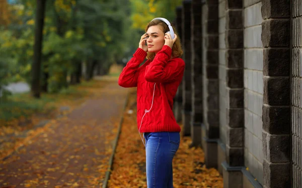 Mulher feliz ouvindo música através de fones de ouvido no parque de outono — Fotografia de Stock