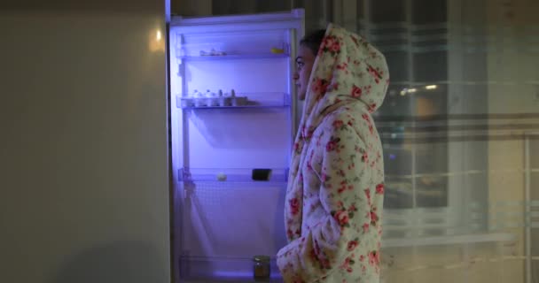 Mladá žena otevře v noci ledničku a vezme si jídlo — Stock video