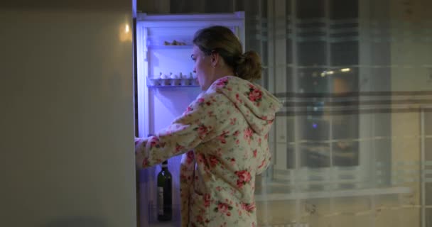 Mujer joven abre el refrigerador por la noche y toma comida — Vídeos de Stock