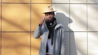 Afrikalı bir adam tuğla arka planda şapka deniyor.