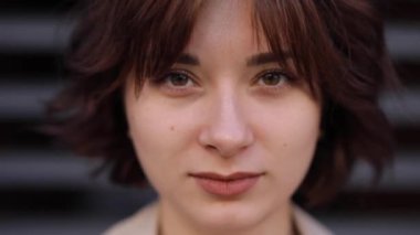 Trençkotlu kadın gözlerini açar ve kameraya bakar.