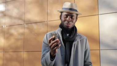 Afro-Amerikalı bir adam dışarıda, akıllı telefonda sohbet ediyor.