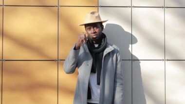 Afrikalı bir adam tuğla arka planda şapka deniyor.