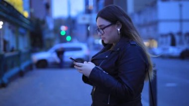 Kadın akıllı telefondan şehrin arka planında sohbet ediyor.