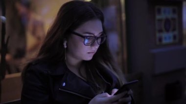 Kadın akıllı telefondan şehrin arka planında sohbet ediyor.