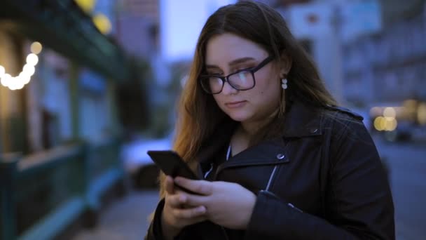 Frau plaudert im Smartphone vor dem Hintergrund der Abendstadt — Stockvideo