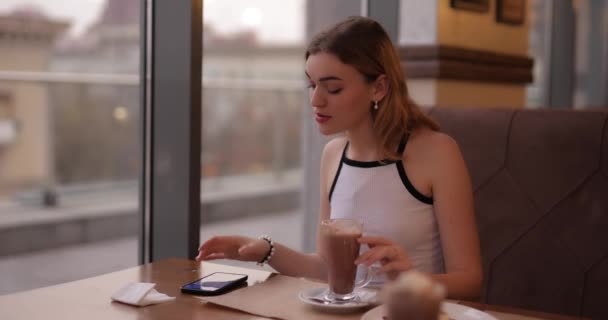 Leuk meisje communiceert in een smartphone aan een tafel in een cafe — Stockvideo