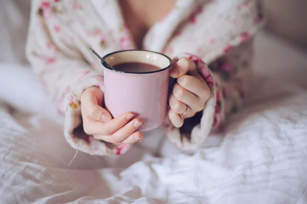 Mains féminines tenant une tasse de thé au lit — Photo