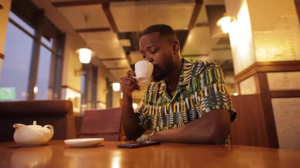Afro-Amerikaanse man op zoek in smartphone en drink koffie — Stockvideo