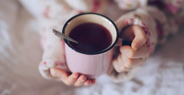 Tangan wanita memegang cangkir dengan teh di tempat tidur — Stok Foto