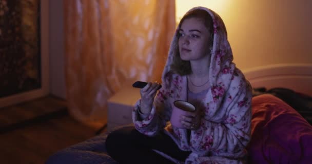 Vrouw zit op bed tv te kijken en thee te drinken — Stockvideo