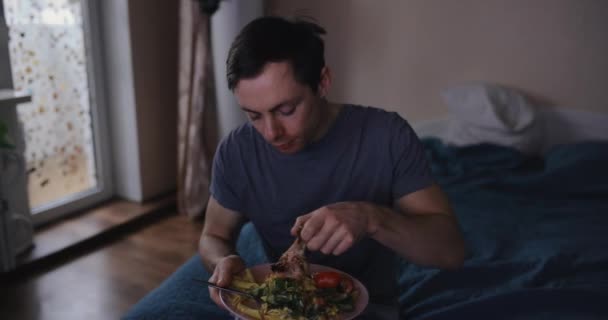 Seorang pria makan daging dan menonton tv di rumah — Stok Video
