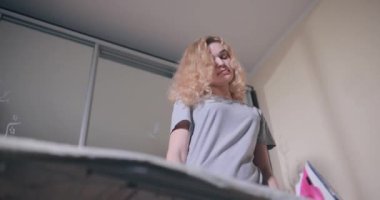 Kadın ütü masasında ütüyle giysileri ütülüyor.