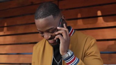 Afro-Amerikalı bir adam dışarıda, akıllı telefonda sohbet ediyor.