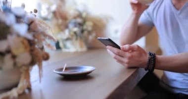 Tanınmayan kişi kahve içer ve akıllı telefon kullanır.