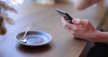 Tanınmayan kişi kahve içer ve akıllı telefon kullanır.