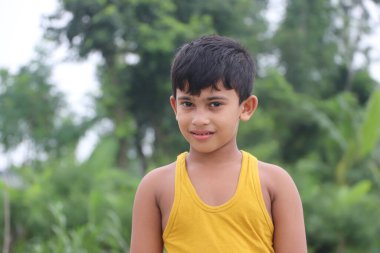 Fotoğraflar için poz veren sevimli, küçük, sağlıklı bir çocuk. Parkta ileriye bakıyor.