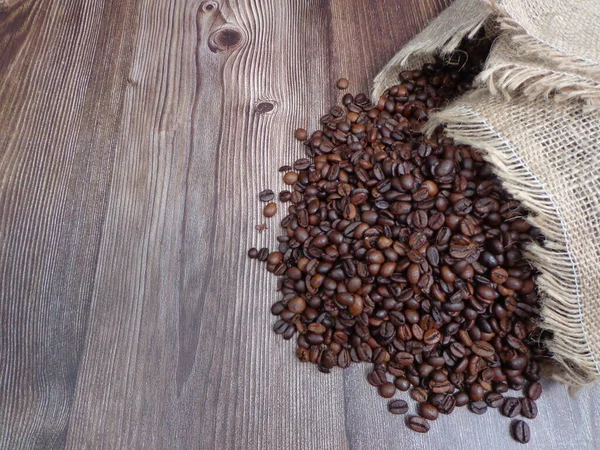 Roasted coffee beans piled up coming out of a cloth sack on a wooden table, with space to place text