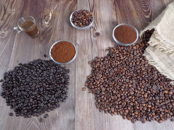 Robes of roasted coffee and intense toast in heaps, accompanied by bowl with ground coffee on a wooden table