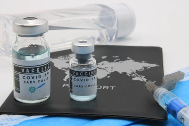 Bir şırınganın yanında maskeli bir pasaport ve iki şişe aşı.