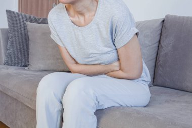  Evde yatarken karın ağrısı çeken genç bir kadın. Mide ağrısı, kadın sorunları. Evde yatakta otururken karın ağrısı.. 