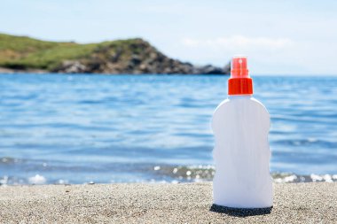 Güneşli bir günde kumlu sahilde, mavi deniz arka planında güneş kremi. Rahatlama kavramı.