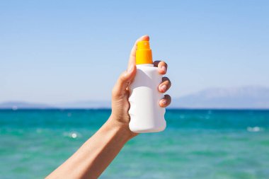 Kadın elinde güneş kremi tutuyor. Güneşli bir gün ve sahilde. Arka planda mavi deniz. Rahatlama konsepti.