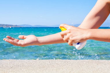 Kadın güneşli kumsalda mavi deniz arka planına güneş kremi sürüyor. Rahatlama konsepti.