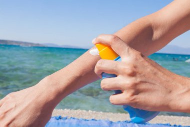 Kadın güneşli kumsalda mavi deniz arka planına güneş kremi sürüyor. Rahatlama konsepti.