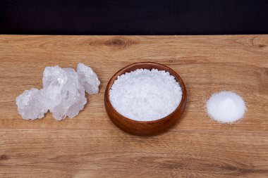 Eski ahşap bir masada ve kırsal bir kasede doğal kaya veya deniz tuzu tanecikleri..