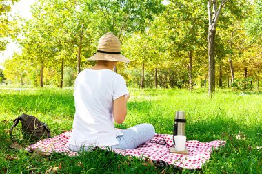 Elinde kitap olan genç bir kadın kırsalda piknik yapıyor. Mutlu, sıcak bir gün, açık havada. Parktaki kadın..
