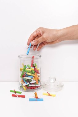 Küçük rulo dilek kağıtları ve beyaz arka planda bir kavanoz. Dilek kavanozu Dilek kavramı. Hayal, arzu, arzu, niyet. Kadın kavanozdan niyetini belli ediyor..