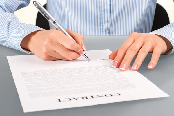 Female signing contract at desk.