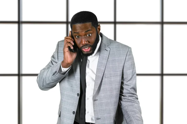 Nerveuze zwarte zakenman die mobiele telefoon vasthoudt. — Stockfoto
