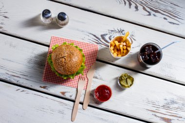 Burger, çatal bıçak takımı ve turşu dilim.