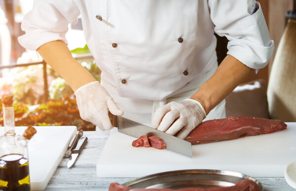 Man cutting meat with knife. Meat lying on cooking board. Preparation of veal in restaurant. Busy morning of skillful chef.