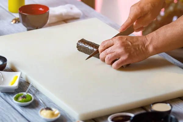 Hand met mes snijdt sushi. — Stockfoto