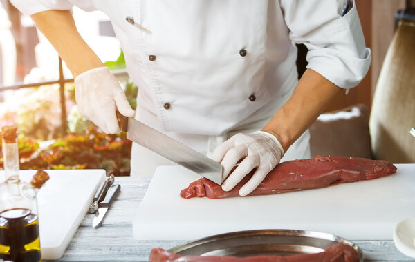 Man cuts meat with knife. Big piece of raw meat. Chef working with veal. Busy morning in the restaurant.