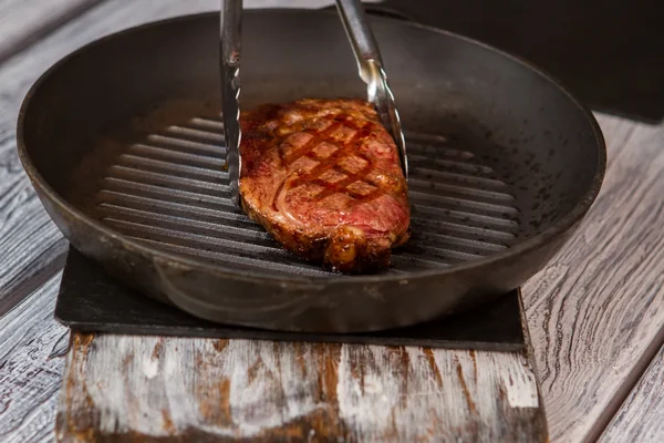 Tongs touch meat on pan. — Stock Photo, Image