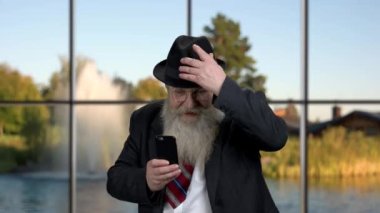 Akıllı telefonunu kullanarak şapka takan kıdemli bir işadamı..