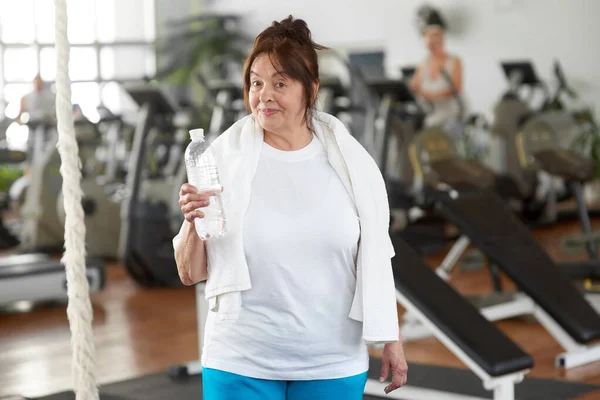 Pretty senior woman with a bottle of water in gym. — Stock Photo, Image