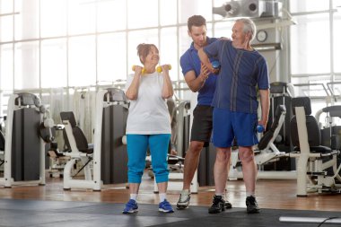Spor salonunda halteri kaldıran son sınıf öğrencisine yardımcı antrenör..