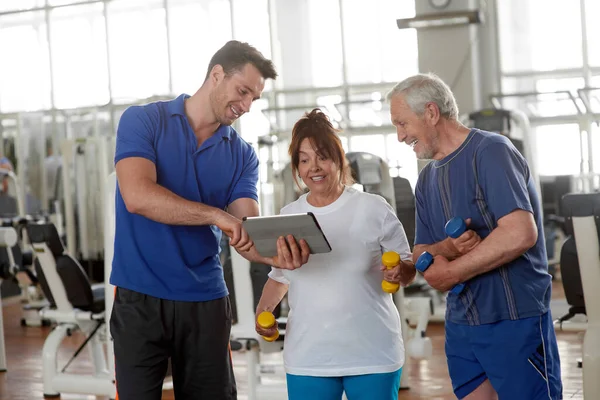 Entrenador personal mostrando ejercicio a personas mayores en el gimnasio. — Foto de Stock