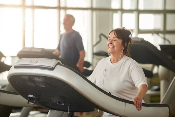 Mujer mayor positiva corriendo en la cinta de correr. — Foto de Stock