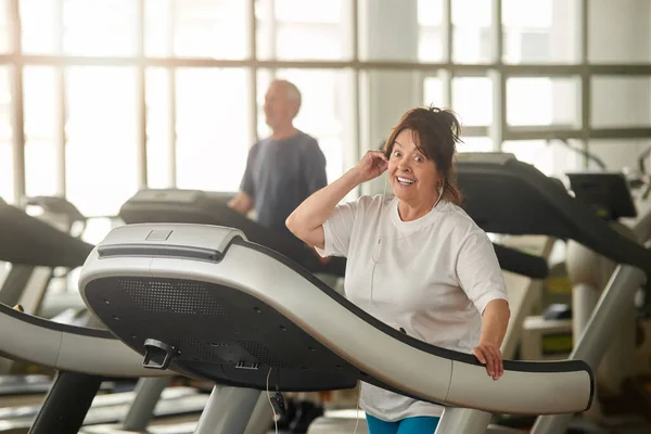 Excited senior woman on treadmill in gym.